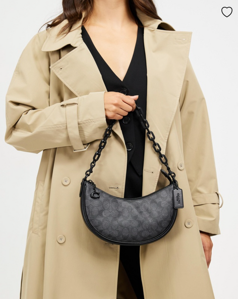 Person wearing a beige trench coat holding a gray handbag with a chain strap on a white background