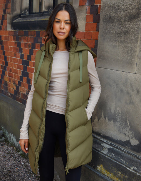 Woman wearing a green puffer vest standing against a textured wall.