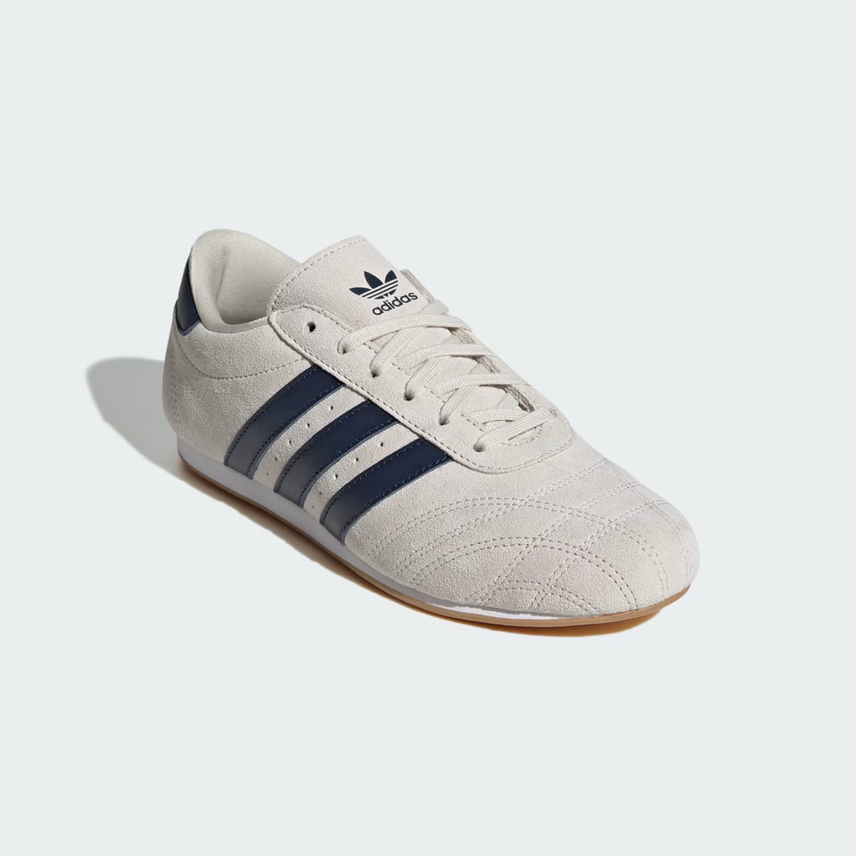 Beige Adidas sneaker with three black stripes on a white background