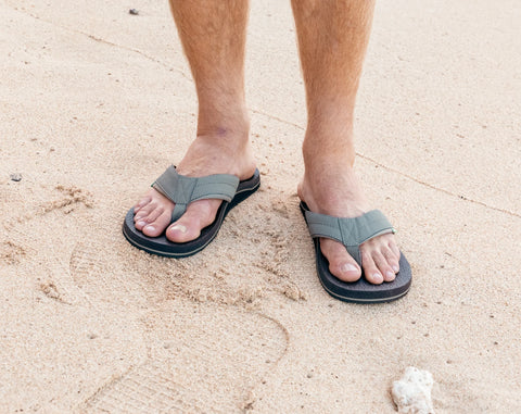 Person wearing gray sandals on a sandy surface
