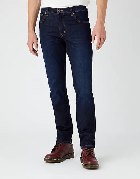 Person wearing dark blue jeans and brown shoes on a white background