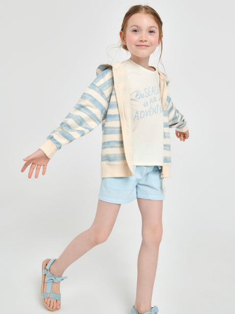 Young girl wearing a striped sweater and light blue shorts on a white background