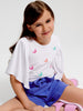 Young girl wearing a white t-shirt with colorful designs and blue shorts on a white background