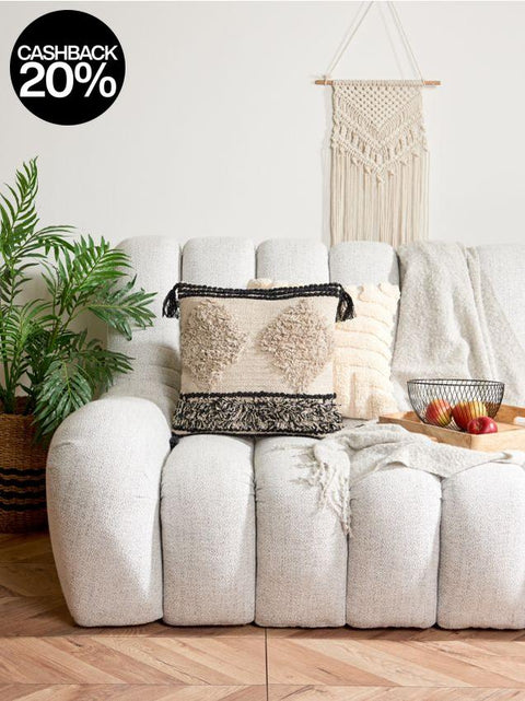 White sofa with decorative pillows and a plant in a room with a macrame wall hanging.