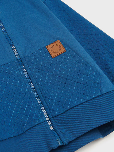 Blue jacket with a brown leather patch on a light gray background
