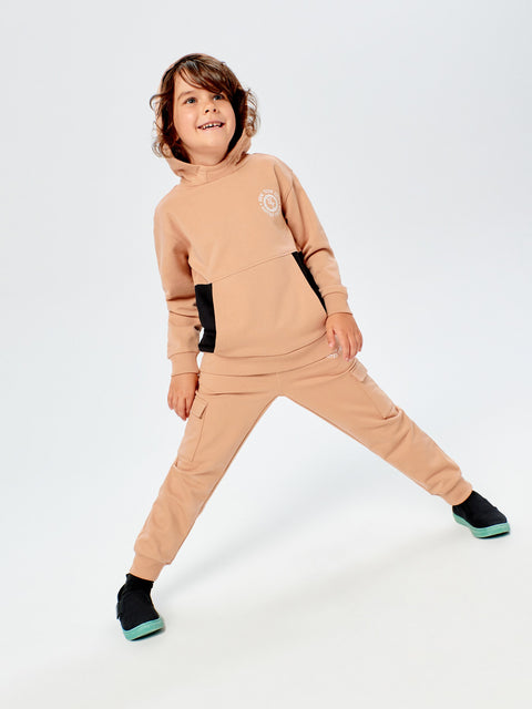 Child wearing a beige tracksuit with black accents on a white background