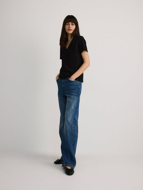 Woman wearing a black top and blue jeans on a plain background