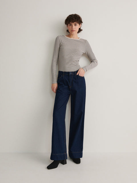 Person wearing a striped shirt and blue jeans on a plain background