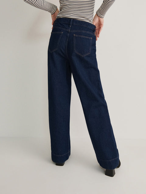 Person wearing dark blue jeans and a striped shirt on a plain background