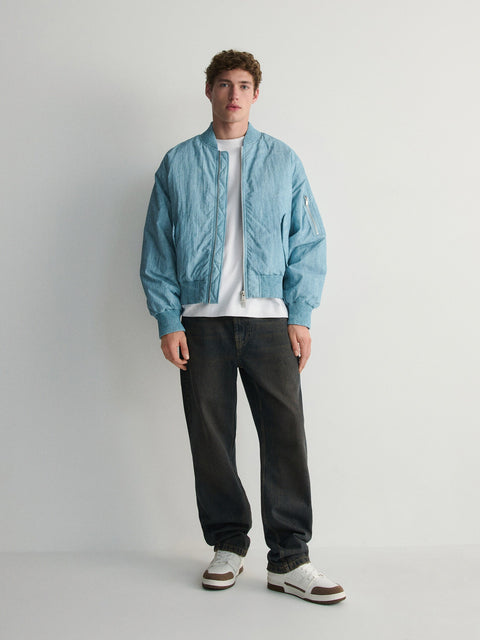 Person wearing a light blue jacket, white shirt, black pants, and white sneakers on a plain background