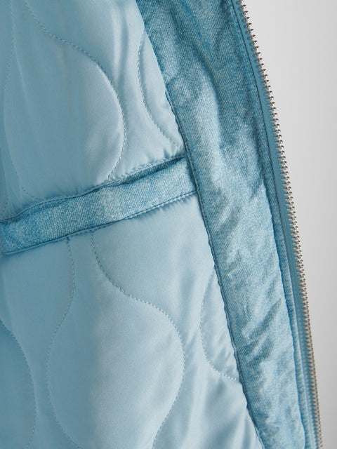 Close-up of a light blue quilted jacket with denim trim on a gray background