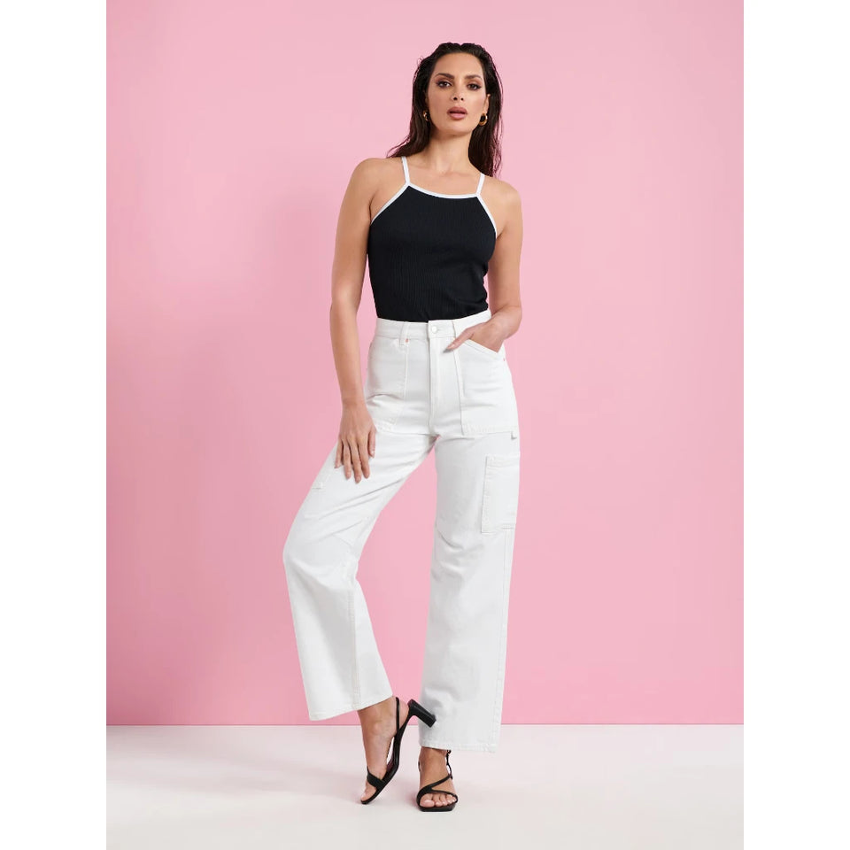 A woman modeling a black halter top with white trim and white wide-leg jeans against a solid pink studio backdrop.
