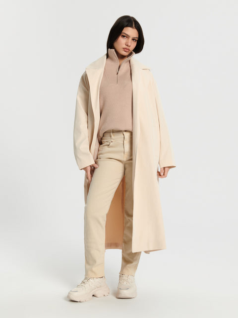 Woman wearing a beige coat over a beige outfit on a white background
