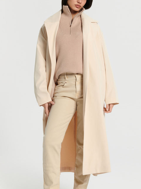 Person wearing a beige coat over a matching outfit on a light gray background
