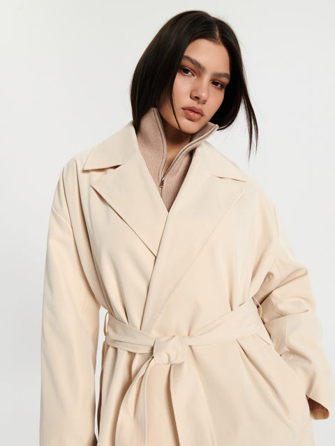 Woman wearing a beige trench coat against a white background