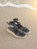Black sandals on a sandy beach with waves in the background