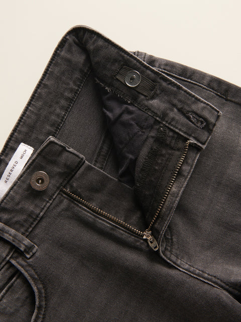 Close-up of black jeans with a zipper and button detail on a beige background