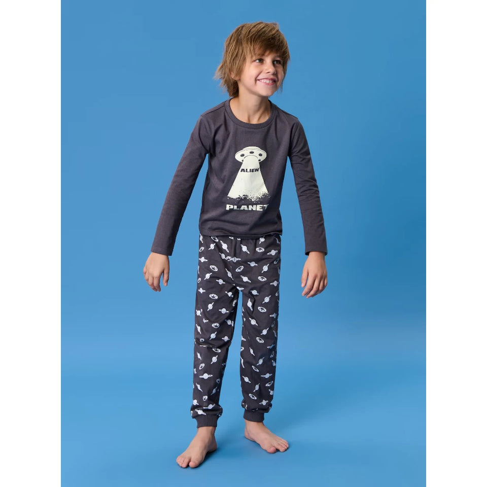 A young boy modeling a dark gray long-sleeve pajama set with a white alien graphic on the shirt and a white space-themed pattern on the pants, standing against a solid blue studio background.