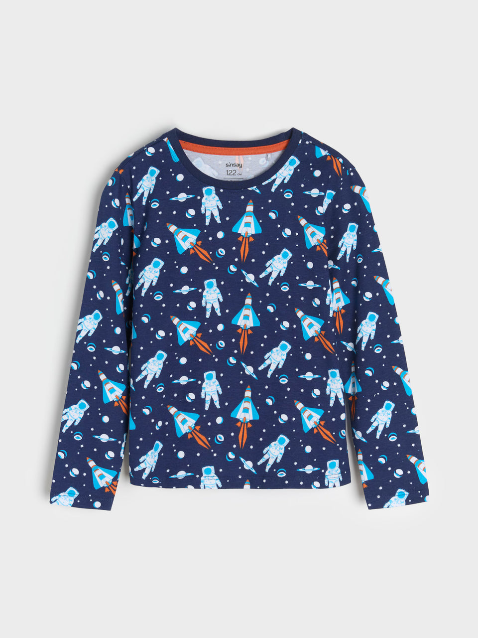 A long-sleeve crewneck shirt for kids, featuring an all-over space-themed print of astronauts and rockets on a navy blue background, shown against a light gray studio backdrop.