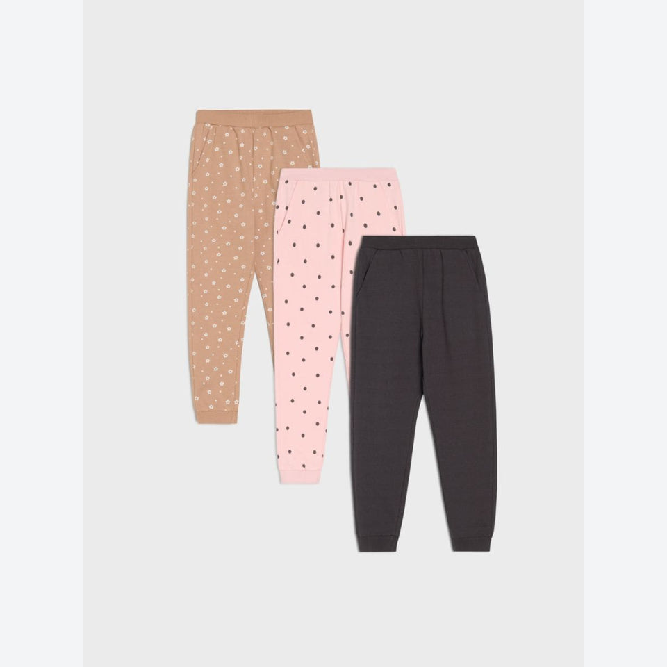 Three pairs of children's jogger pants displayed flat against a light gray background. The set includes tan pants with white polka dots, light pink pants with dark pink polka dots, and dark charcoal gray pants with no pattern.