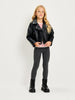 A young girl stands against a light gray studio background wearing a black faux-leather moto jacket, a red and white striped long-sleeve shirt, dark gray leggings, and black lace-up boots.