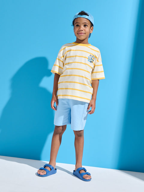 Child wearing a striped shirt, shorts, and sandals against a blue background