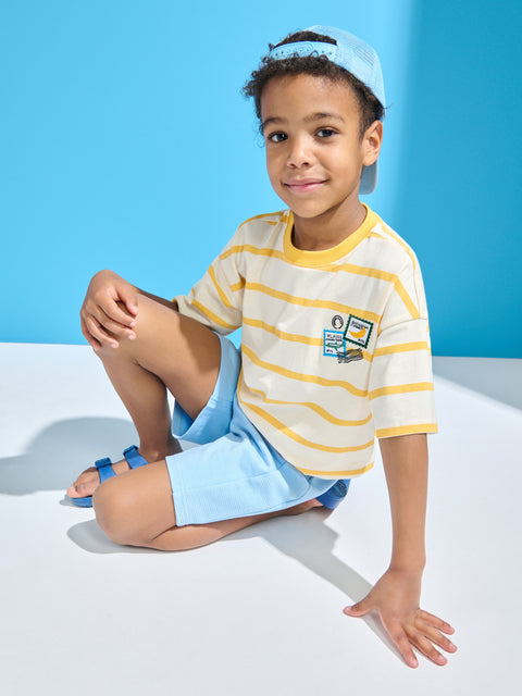 Child wearing a striped shirt and shorts sitting on a white surface with a blue background