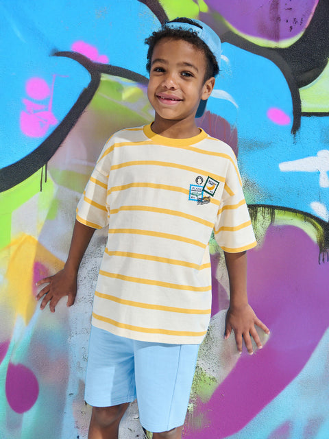 Child wearing a striped shirt with a logo in front of colorful graffiti