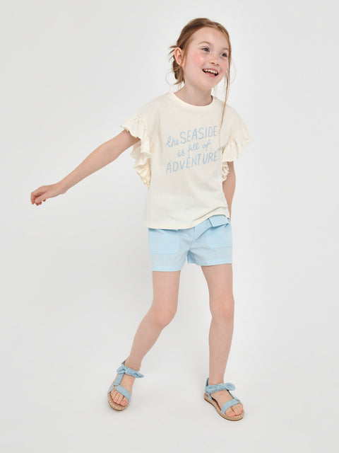 Young girl wearing a light-colored t-shirt and blue shorts on a white background