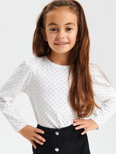 Young girl wearing a white polka dot blouse with a plain background