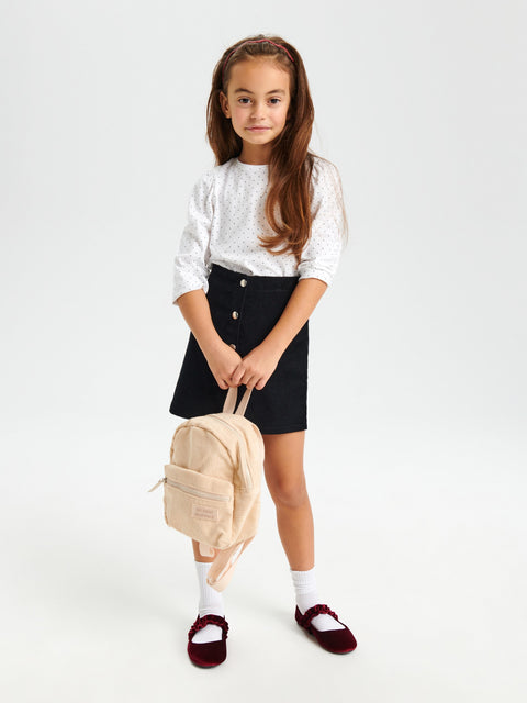 Young girl holding a beige backpack against a white background