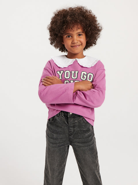 Child wearing a pink sweater with text and gray pants on a white background