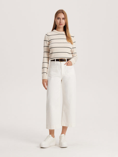 Woman wearing a striped sweater and white pants on a plain background