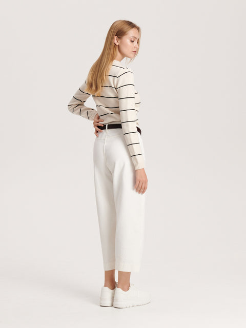 Woman wearing a striped sweater and white pants on a light gray background