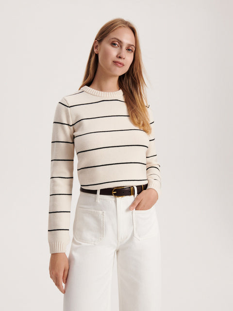 Woman wearing a striped sweater and white pants on a plain background