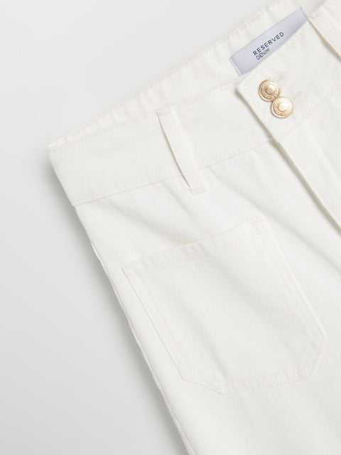 Close-up of a white blazer with a button and label on a light gray background