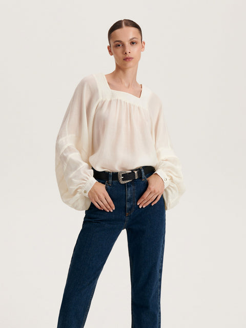 Woman wearing a white blouse and blue jeans on a plain background