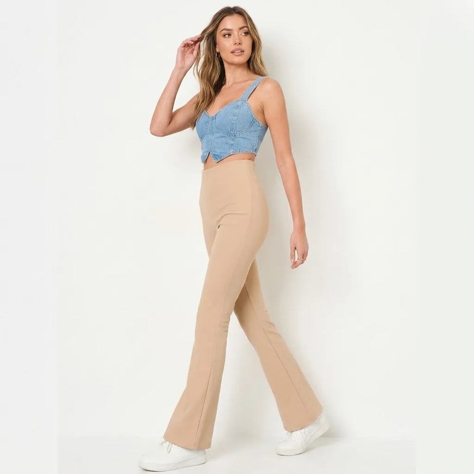 A woman modeling a two-piece outfit consisting of a light blue denim crop top and beige high-waisted flared pants, paired with white sneakers, against a plain white studio background.