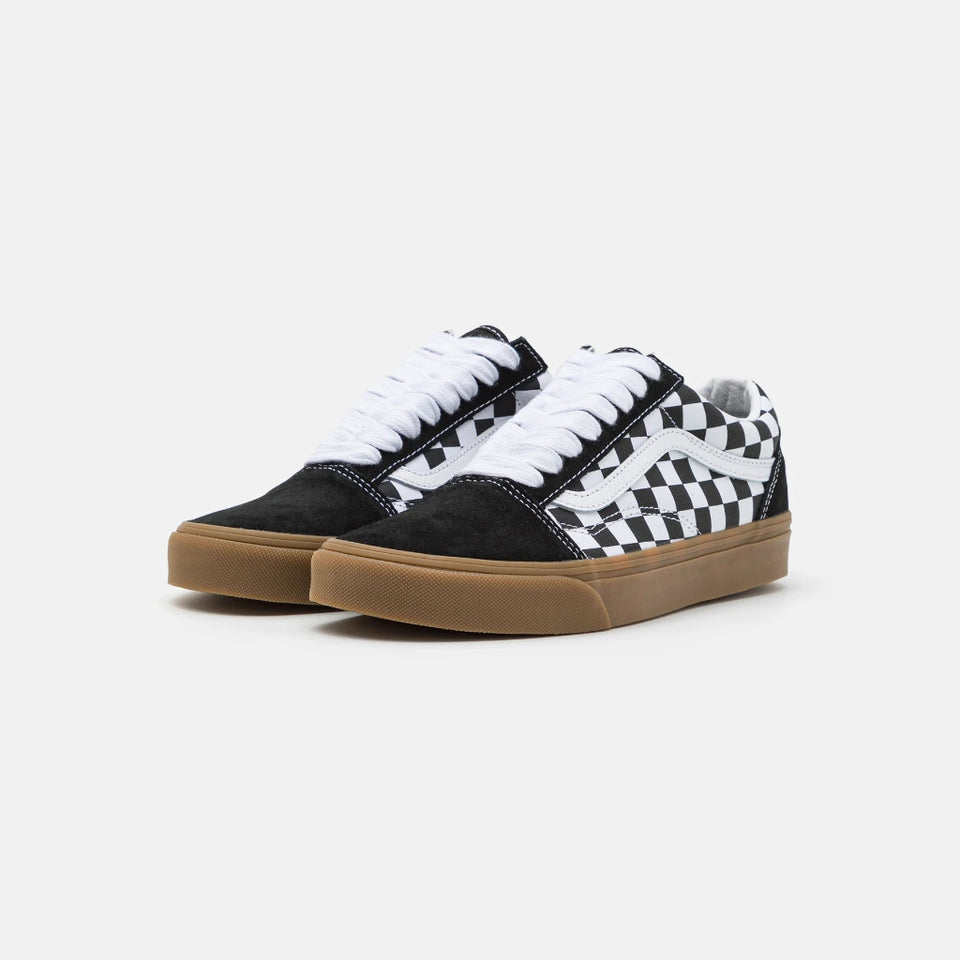 A pair of low-top Vans sneakers featuring a black and white checkerboard pattern on the side, black suede uppers, white laces, and a brown gum sole, set against a plain light gray background.