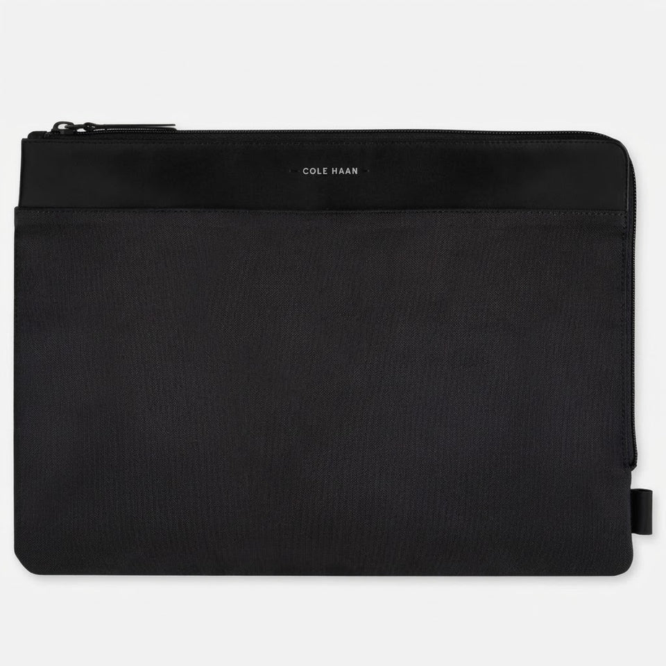 A black Cole Haan zippered pouch with a textured fabric body and a smooth black top band featuring the brand name in white, shown on a light gray background.