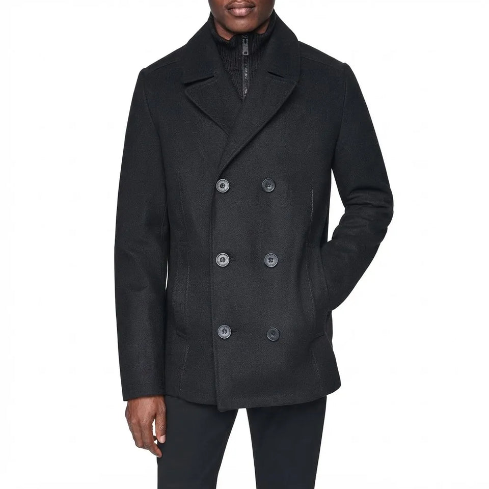 A man wearing a black double-breasted peacoat over a black zippered sweater, shown from the chin down against a plain white background.