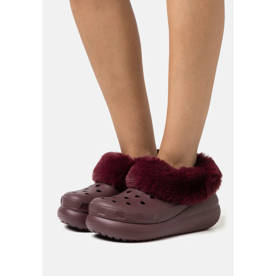 A person wearing burgundy faux-fur clogs with a matching burgundy sole, shown from the calves down against a light gray background.