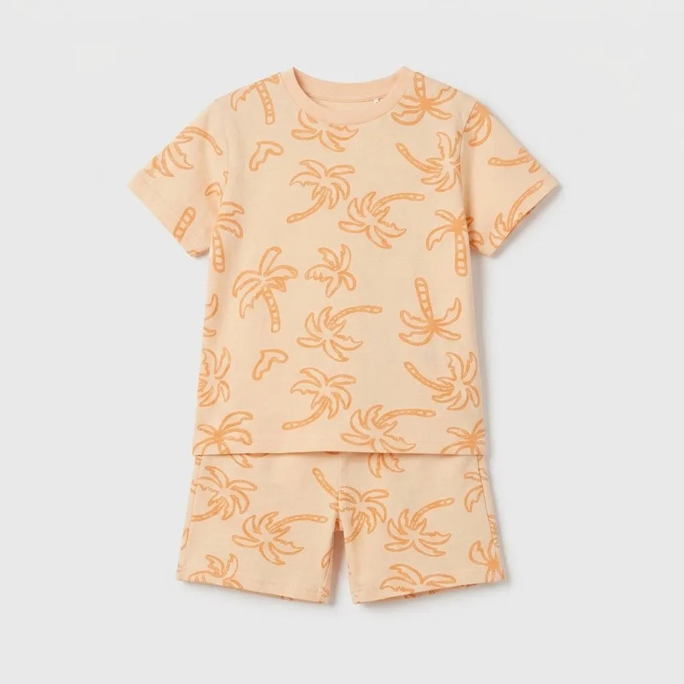 A two-piece kids' pajama set featuring a short-sleeve top and matching shorts in a light peach color with an orange palm tree pattern, displayed flat against a light gray background.