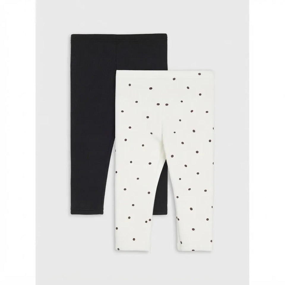 Two pairs of children's leggings displayed flat against a light gray background. The pair on the left is solid black, and the pair on the right is off-white with a scattered small dark polka dot pattern.