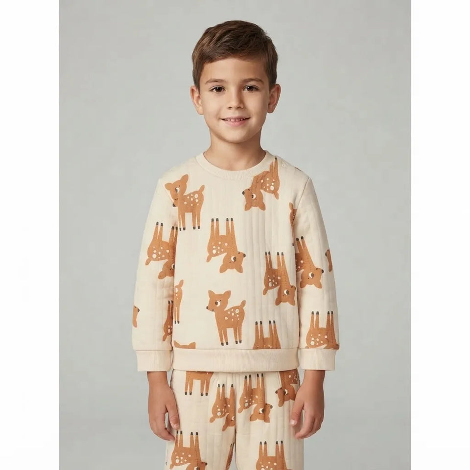 A young boy wearing a cream-colored ribbed long-sleeve pajama top and matching pants, both featuring an all-over print of brown and orange foxes, standing against a neutral gray background.