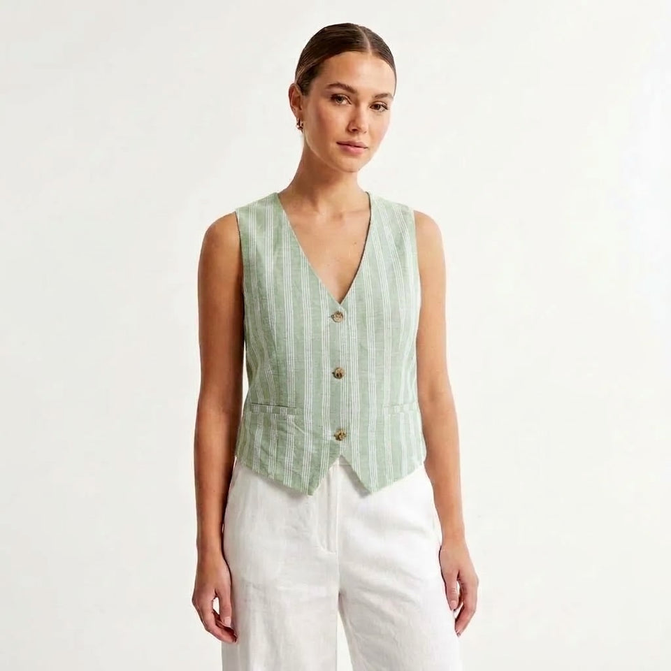 A woman modeling a sleeveless light green and white vertically striped vest with a V-neck and three front buttons, paired with white pants, against a plain white studio background.