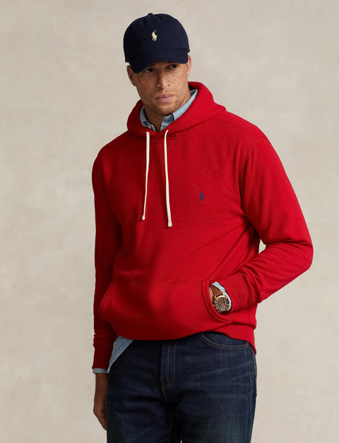 Man wearing a red hoodie and navy cap with a logo on a beige background