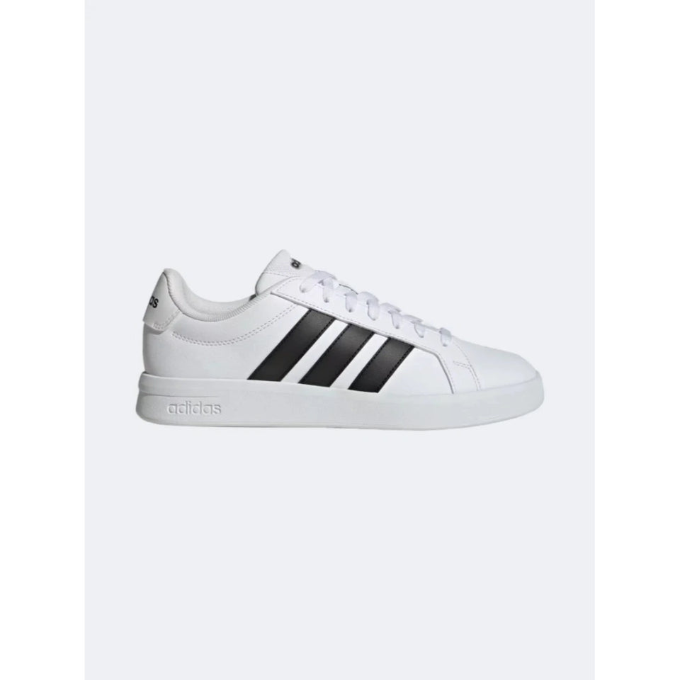 A white Adidas low-top sneaker with three black stripes on the side, white laces, and a white rubber sole, shown from a side profile view against a light gray background.