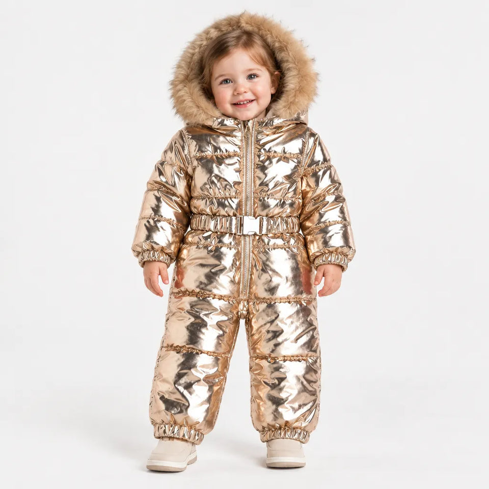 A toddler wearing a shiny metallic gold puffer snowsuit with a faux-fur trimmed hood, standing against a plain light gray studio background.