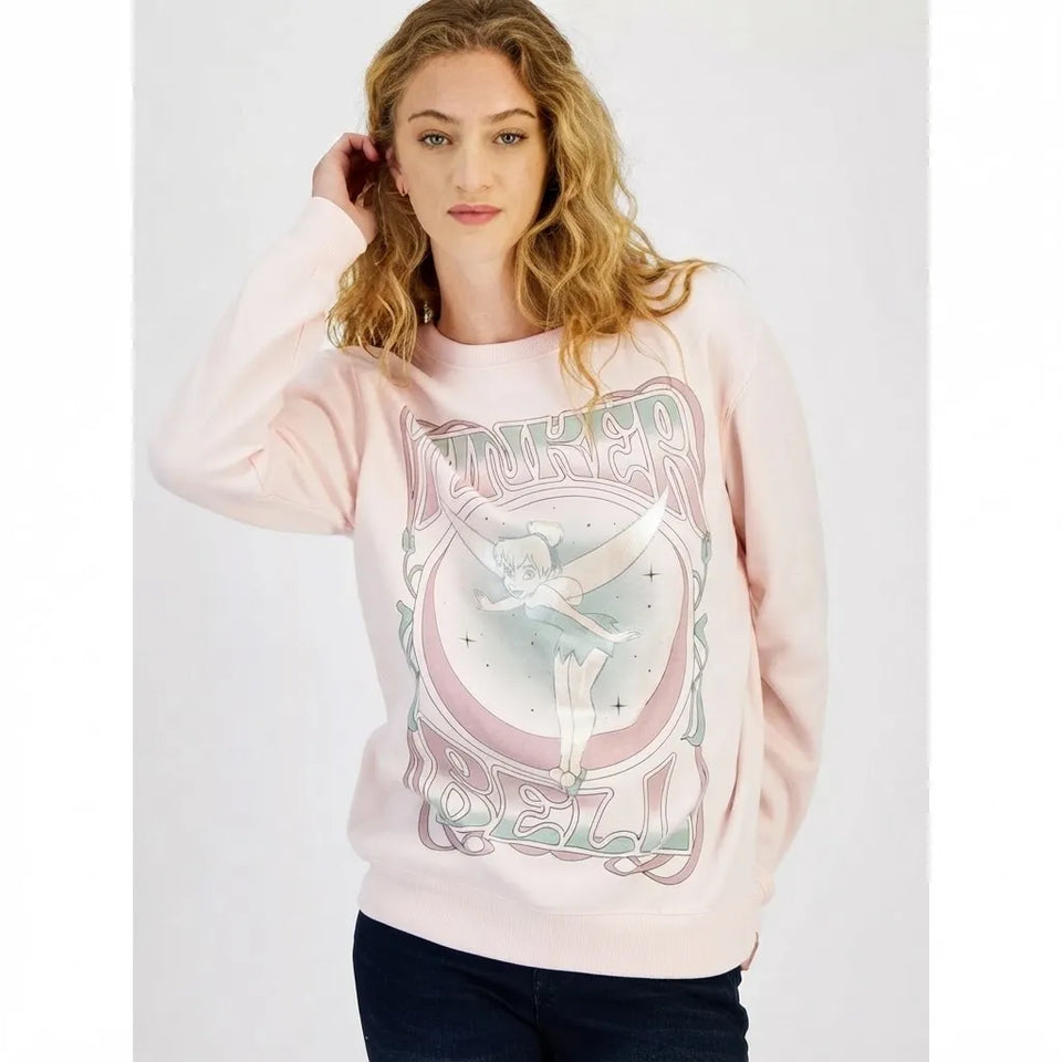 A woman wearing a light pink crewneck sweatshirt with a large graphic print of Tinker Bell on the front, paired with dark jeans, against a plain light gray background.